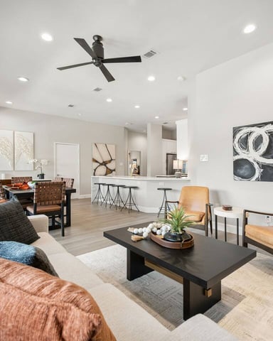 Open-plan living room with cream sofa, tan leather chairs, black coffee table, and kitchen bar with stools in background