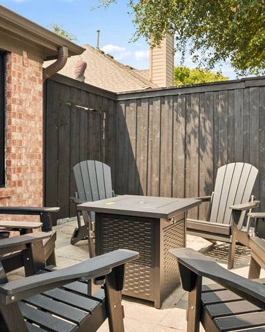 Brick patio with Adirondack chairs, fire table, and dark wooden privacy fence surrounding seating area