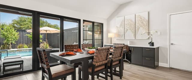 Modern dining room with black table, woven chairs, and floor-to-ceiling windows overlooking backyard pool